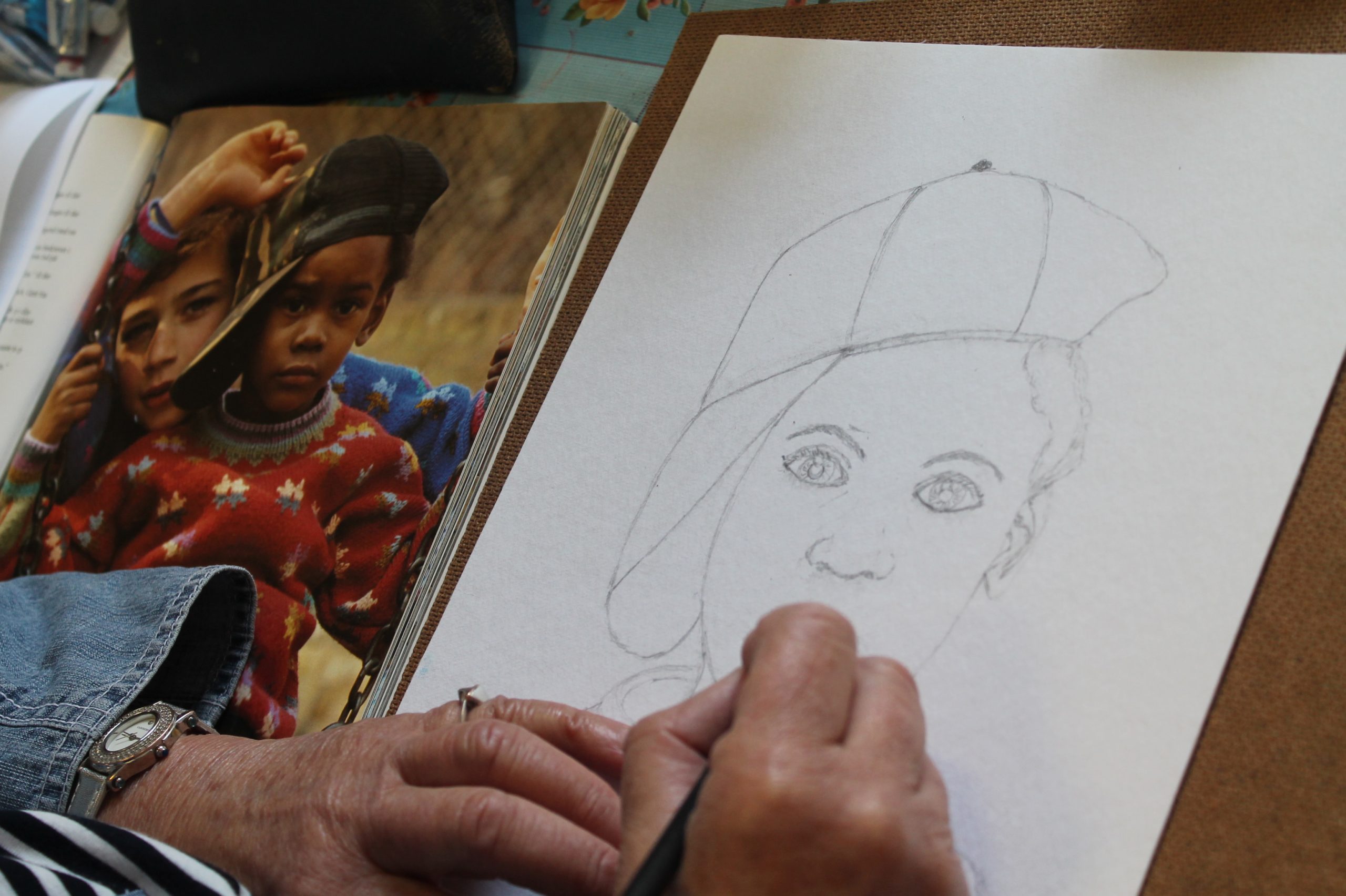 A photograph of someone's hands drawing a picture of a woman's face with a pencil
